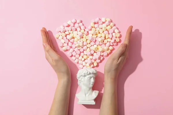 Heart made of marshmallow, ancient head and female hands on pink background