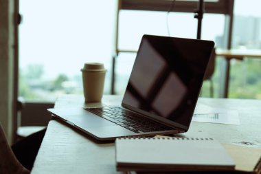 Kahve, dizüstü bilgisayar ve ofis kağıtları olan ofis masası, not defterleri.