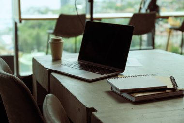 Bir dizüstü bilgisayar, belgeler, defterler ve masanın üzerinde bir fincan kahve.