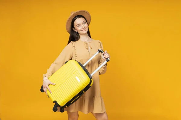 黄色の背景にスーツケースを着た若い女性 — ストック写真