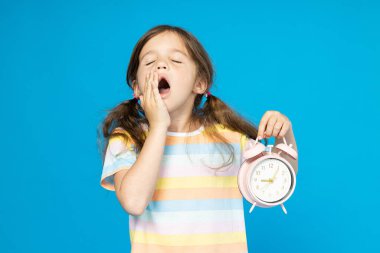 Elinde çalar saati olan küçük bir kız uyumak istiyor.
