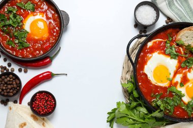 Beyaz arka planda Shakshuka, havlu, baharat, kırmızı biber ve pide olan tavalar, metin için yer