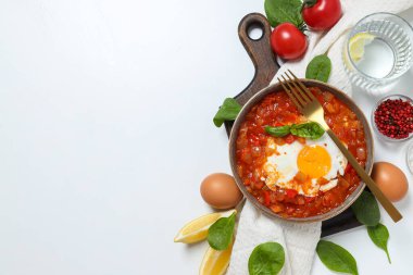Shakshuka güvertede, çatal, havlu ve malzemeler beyaz arka planda, metin için boşluk