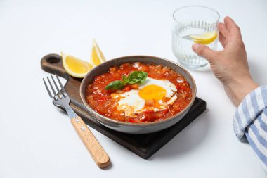 Shakshuka gemide, limon, beyaz arka planda erkek elinde bir bardak su.