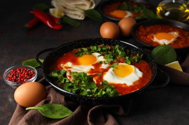 Shakshuka, yumurta, fesleğen, koyu arkaplanda bir kase biber ve yağ.
