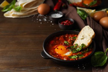 Shakshuka tavada, bir parça ekmek, limon, fesleğen, tuzlu kase, ahşap zemin üzerinde, metin için yer