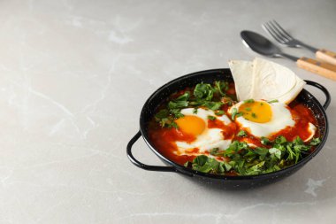 Shakshuka ve Pita in pan, spoon and fork on light background, space for text