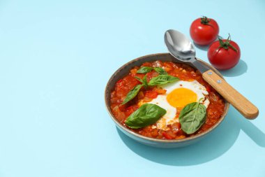 Bir kase shakshuka, kaşık ve mavi arka planda iki domates, metin için yer