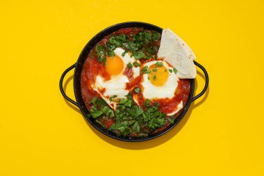 Shakshuka tavada ve Pita sarı arkaplanda, üst manzara