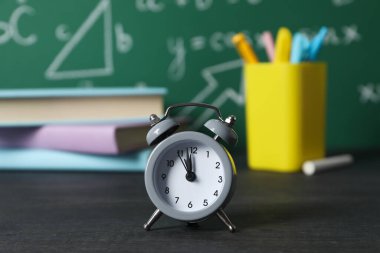 Okul malzemelerinin arka planındaki masanın üzerindeki saat.