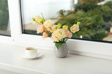 Bir demlik kahve ve pencere eşiğinde şehir manzaralı bir vazo çiçek.