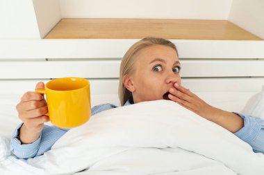 Elinde çayıyla battaniyenin altında neşeli bir kadın.