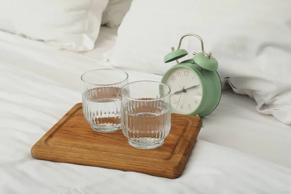 Morning water on a board with an alarm clock, in bed