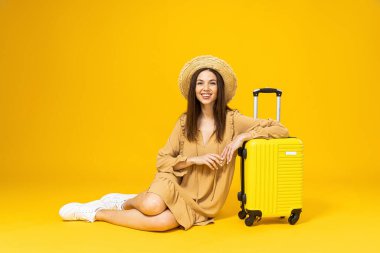 Plaj şapkalı genç bir kadın ve sarı arka planda bir valiz.