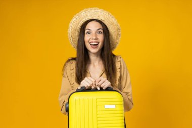 Plaj şapkalı genç bir kadın ve sarı arka planda bir valiz.