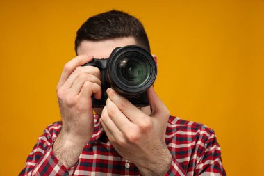 Bir adam fotoğraf çekiyor, bir fotoğrafçı, sarı arka planda.