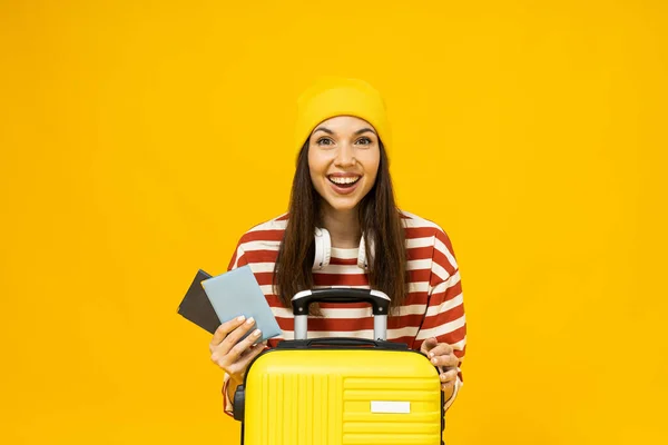 stock image Happy young woman in striped t-shirt with suitcase and tickets on yellow background