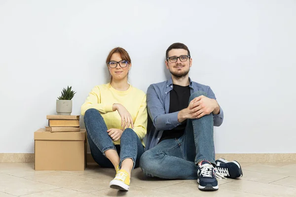 一对夫妇坐在一间空荡荡的公寓的地板上 手里拿着箱子 — 图库照片