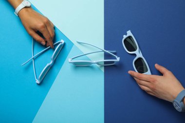 Mavi güneş gözlüğü ve kadın eli mavi arka planda, üst manzara