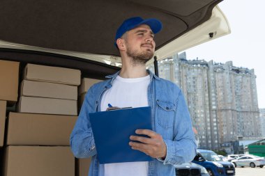 Elinde klasör olan bir kurye kutuları olan bir arabanın yanında.