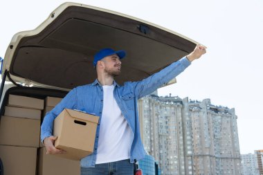 Kutuları olan bir arabanın yanında elinde kutu olan bir kurye.