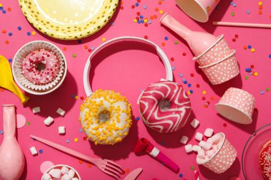 Donutlar, kulaklıklar ve parti malzemeleri pembe arka planda, üst manzara