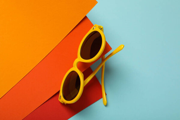 Orange sunglasses on red and orange paper on blue background, space for text