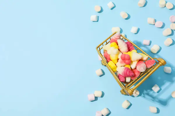 stock image Jelly candies in shopping trolley on blue background, space for text