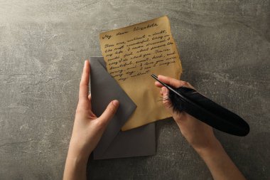 Üzerinde yazı, gri zarf ve gri arkaplan üzerinde tüy olan mektup, üst görünüm