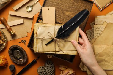 Ellerinde eski harfler ve tüy olan ahşap kutu, turuncu arka planda antika kağıtlar ve hediyelik eşyalar, üst manzara.