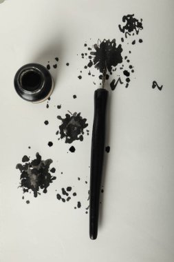 Beyaz arka planda mürekkep lekeleri, kalem ve mürekkep şişesi, üst manzara.