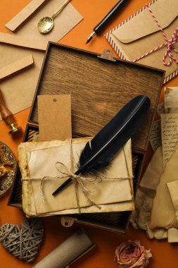 Eski harfler ve tüy ile ahşap kutu, turuncu arka planda antika kağıtlar ve hediyelik eşyalar, üst manzara