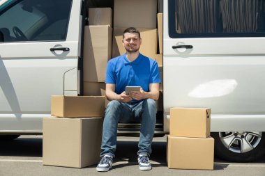 Elinde tablet olan bir kurye kutuları olan bir arabanın yanında.