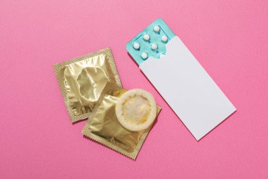 Pembe arka planda prezervatif ve doğum kontrol hapları, metin için yer