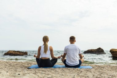 Bir çift deniz kıyısında meditasyon yapıyor.