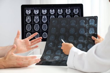 Doktor beyin tümörünü MRI görüntülerinde hastaya gösteriyor.