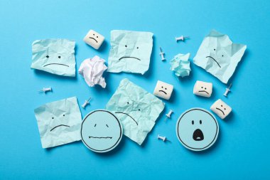 Kağıtlar ve şekerlemeler mavi arka planda üzgün emoji, üst manzara
