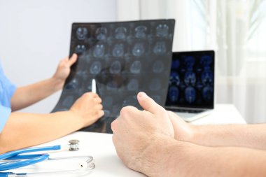 Doktor beyin tümörünü MRI görüntülerinde hastaya gösteriyor.