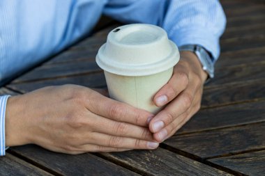 Kağıt bardak, kadın eli, tahta arka planda.