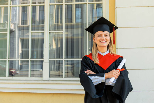 Улыбающаяся молодая женщина в мантии и шляпе в городе, место для текста