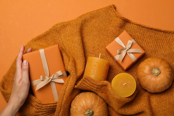 Candles, boxes and pumpkin on sweater, female hand on orange background, top view