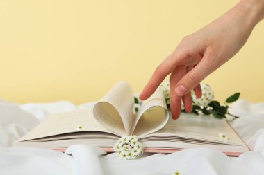Sarı arka planda çiçek ve kadın eli olan açık bir kitap