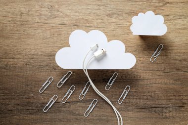Beyaz USB kabloyla beyaz kağıt bulutlar ve tahta arka planda metal ataçlar.