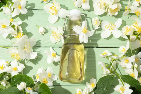 Jasmine flowers and glass bottle on green wooden background, top view