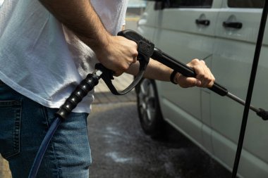 Bir adam oto yıkamada araba yıkar.