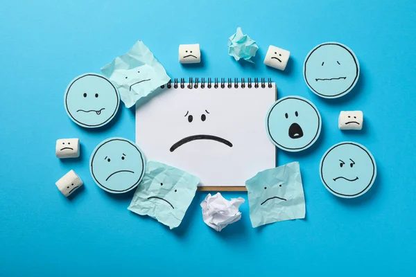 Notizblock Und Papiere Mit Traurigen Emojis Auf Blauem Hintergrund Draufsicht — Stockfoto
