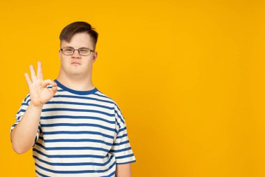 Serebral felçli, sarı arka planda çizgili tişörtlü, gözlüklü gülümseyen genç adam. Dünya Genetik Hastalıklar Günü konsepti, metin için yer