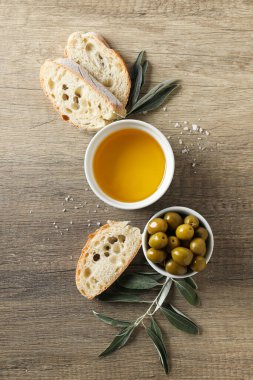 Zeytinyağı, zeytin ve ekmek dilimleri ahşap arka planda, üst manzara