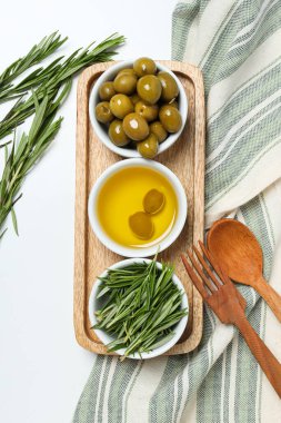 Zeytin dalları, yağlar ve zeytinler kaselerde, beyaz arka planda havlu, üst manzara