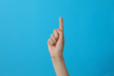 Mavi arka planda bir parmağını gösteren kadın eli